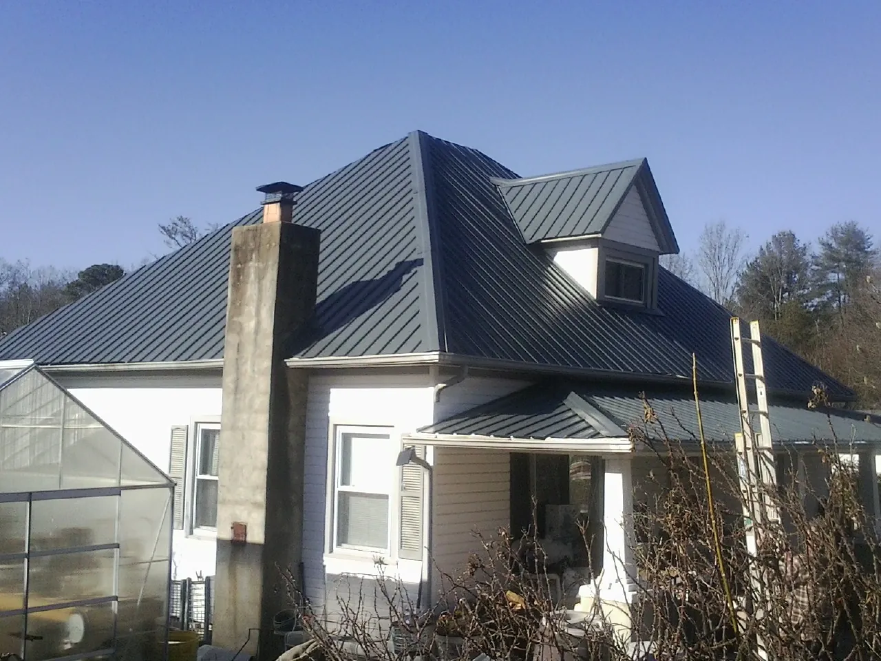 Dark blue standing seam metal roof on a white farmhouse with dormer — Slate & Tile Roof Repair by Roofing Brothers in Mack