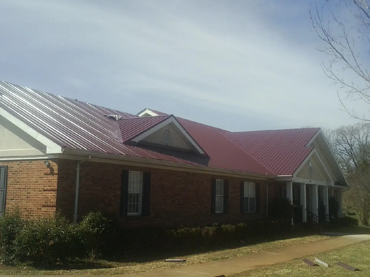 Red metal roof with gabled entries on a long brick building, from a Hail Damage Roof Repair job in Mack