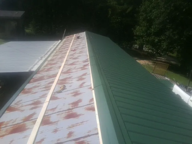 Old rusted panels beside newly installed green metal roofing — Wind Damage Roof Repair by Roofing Brothers in Mack