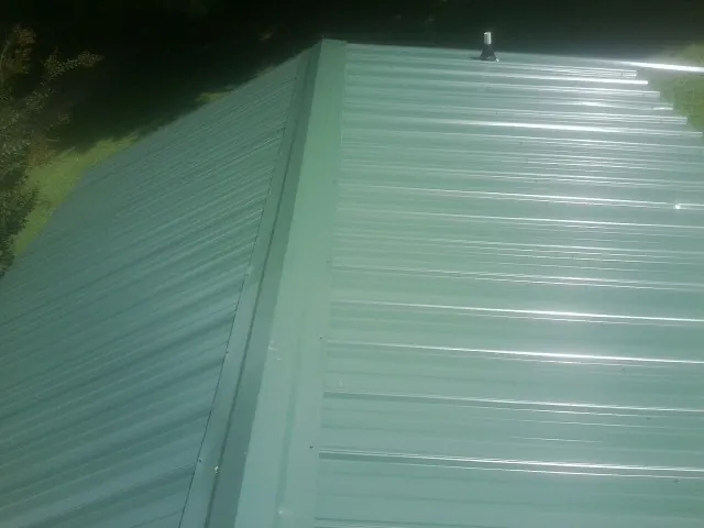 New green metal panels meeting at the ridge of a roof — Flat Roof Repair work by our crew in Mack