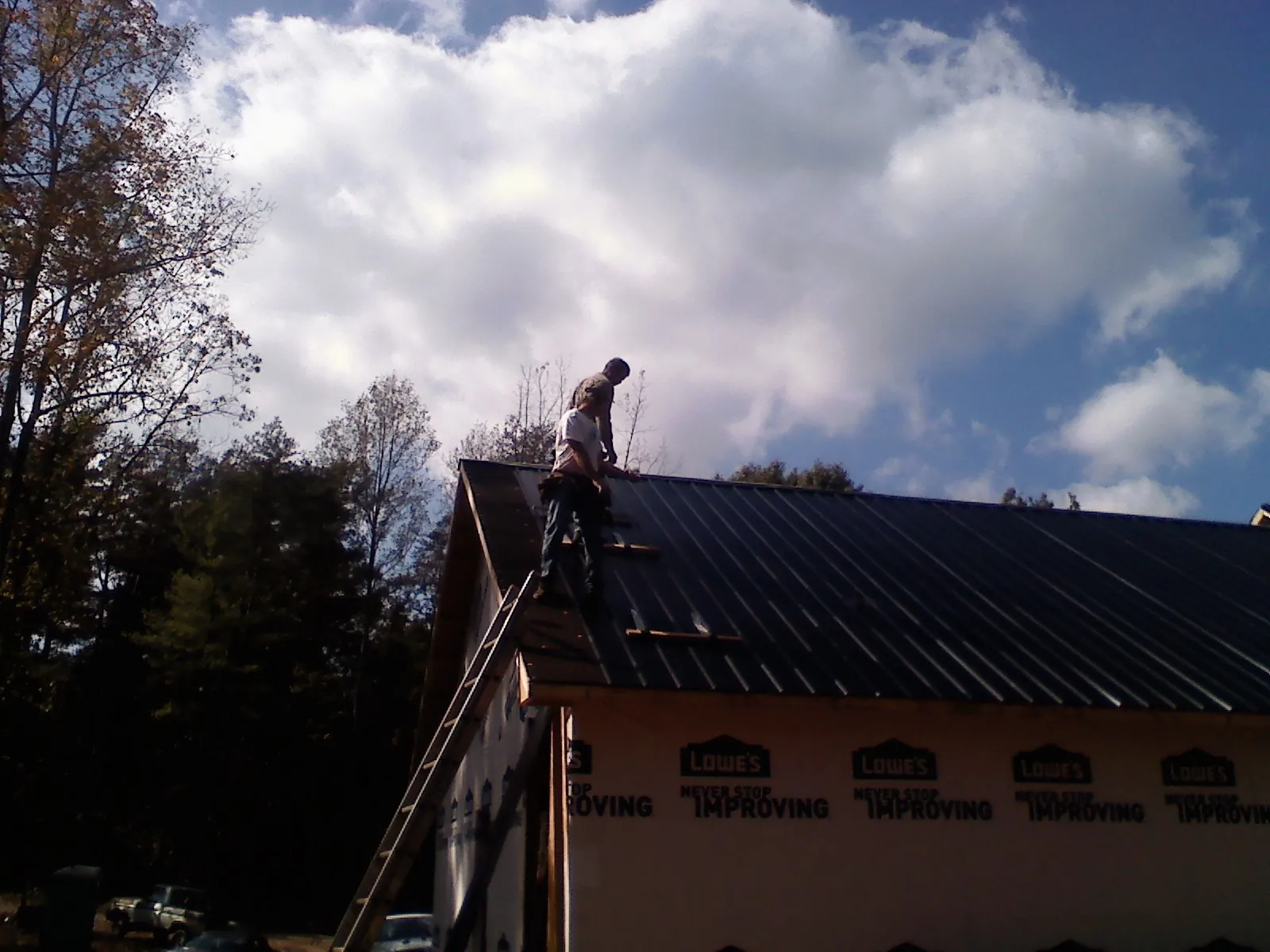Roofer fastening dark metal panels high against a cloudy sky, from a Roof Inspection job in Mack