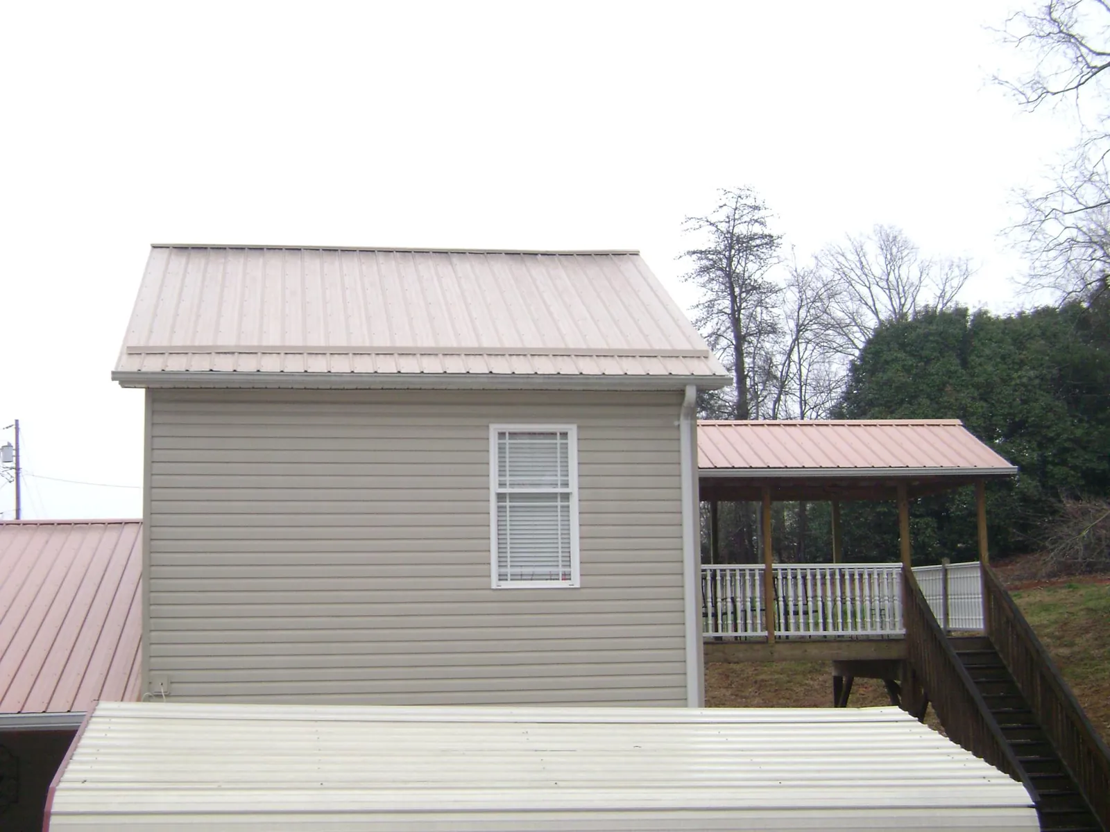 Tan metal roofs on a two story addition and attached porch, from a Roof Replacement job in Mack